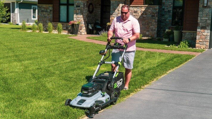 A man precisely edges a lawn in dry conditions using a Trimyxs attached to a push mower, exploring the best time to edge.