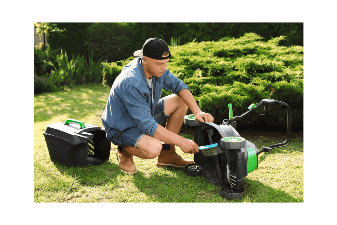 Person cleaning an electric lawn mower in a grassy area
