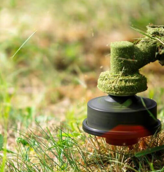 A grass trimmer head against green grass background 